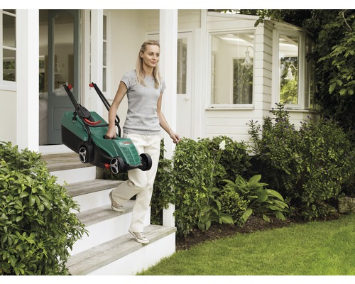Eine Frau trägt einen Rasenmäher auf einer Treppe vor einem Haus.