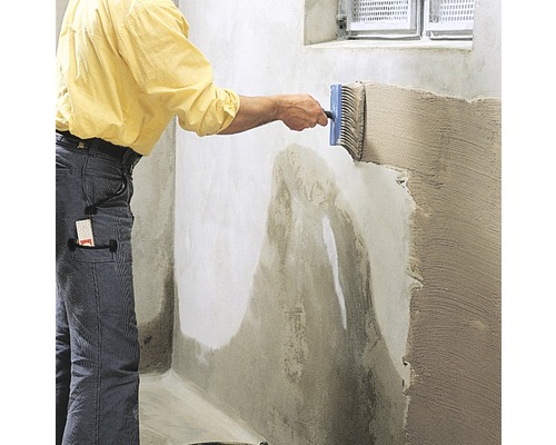 Mann trägt mit Flächenstreicher eine Abdichtung auf eine Wand auf