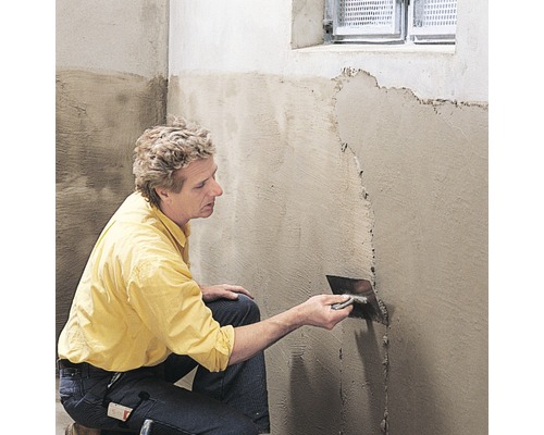 Eine Person trägt Putz mit einer Glättkelle auf eine Wand auf.