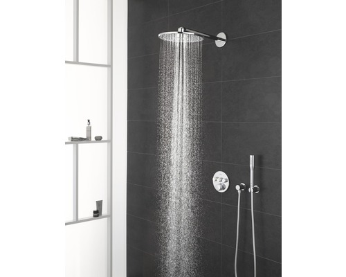 Regendusche mit Wasserstrahl und Armaturen an einer dunklen Wand im Badezimmer.