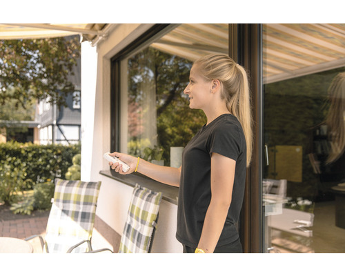 Frau bedient Markise mit Fernbedienung auf Terrasse