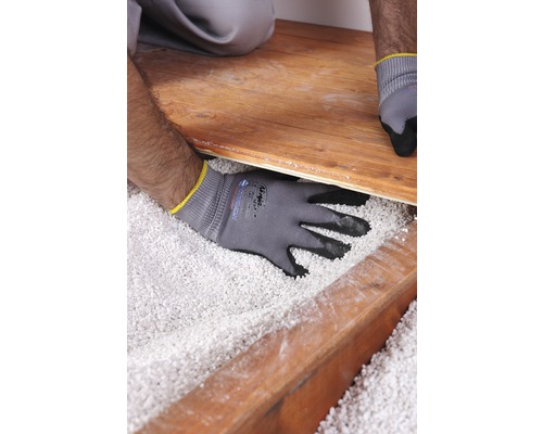 Ein Handwerker verlegt Holzboden über einer Schüttung aus Dämmstoff.