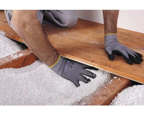 Ein Arbeiter mit Arbeitshandschuhen verteilt Schüttdämmung unter einem Holzboden.