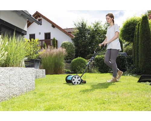 Frau benutzt einen Spindelmäher im Garten.