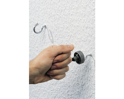 Hand dreht eine Schraube in eine Wand neben einem Haken