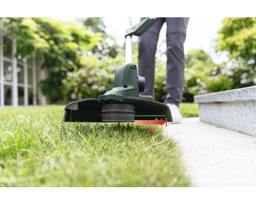 Person schneidet Rasen mit einem Rasentrimmer im Garten.