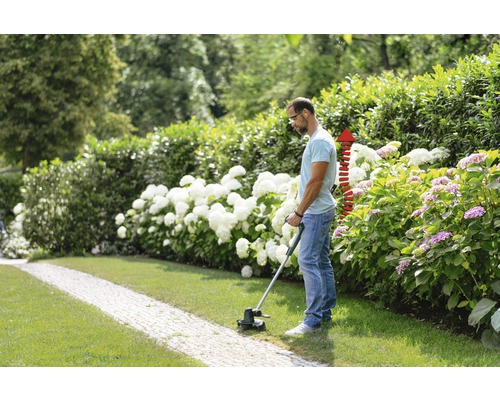 Mann schneidet Rasen mit Rasentrimmer im Garten.