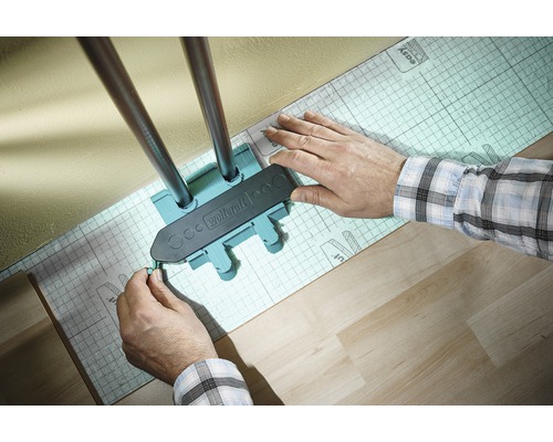 Wolfcraft Logo. Eine Person verwendet eine Anreißlehre zum Anzeichnen von Heizungsrohren auf einer Dämmunterlage.