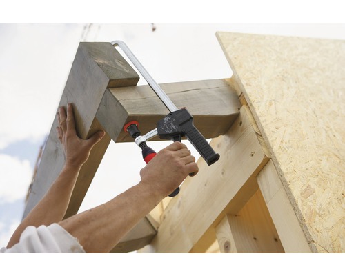 Eine Person befestigt Holzbalken mit einer Schraubzwinge an einem Holzrahmen.