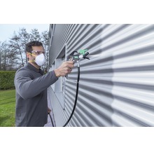 Mann mit Schutzbrille und Maske beim Sprühlackieren einer Wand mit einem Farbsprühgerät
