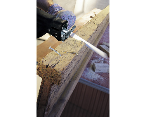 Eine Stichsäge schneidet ein Holzbrett mit Nägeln.