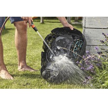 Eine Person reinigt einen Rasenmähroboter mit einem Wasserschlauch auf einer Rasenfläche.