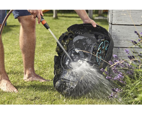 Eine Person reinigt einen Rasenmähroboter mit einem Wasserschlauch auf einer Rasenfläche.