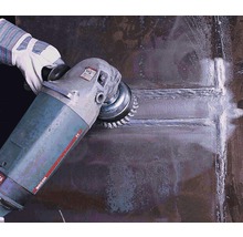 Eine Person verwendet eine Drahtbürste an einer Schleifmaschine zum Reinigen einer Metalloberfläche.