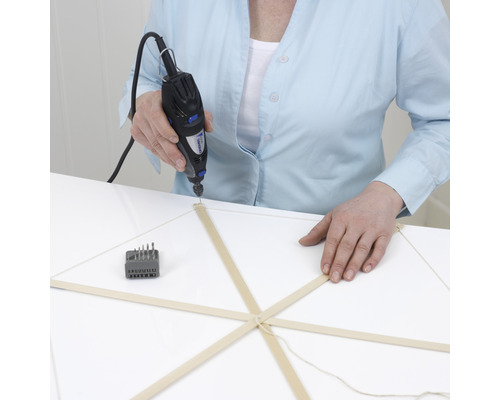 Eine Person bohrt mit einem Dremel Multifunktionswerkzeug ein Loch in einen Holzstab.