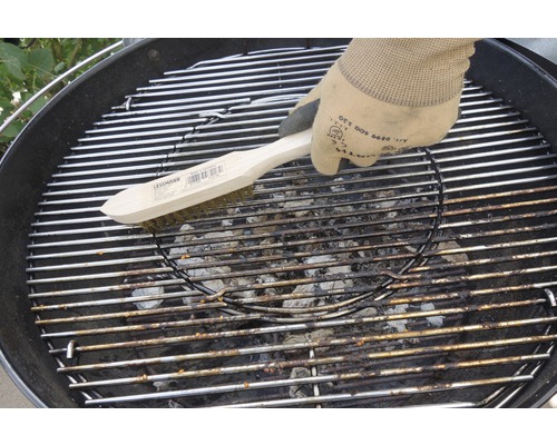 Eine Person reinigt mit einer Grillbürste einen Grillrost.