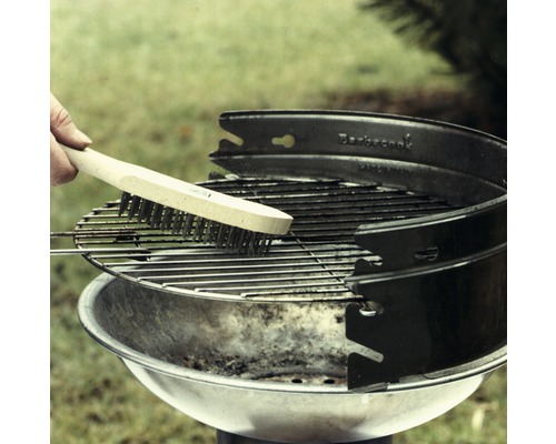 Eine Person reinigt einen runden Grillrost mit einer Grillbürste.