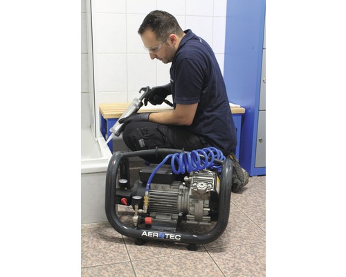 Handwerker verwendet eine Kartuschenpistole und einen Kompressor im Badezimmer.