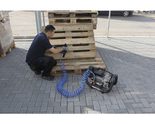 Ein Mann arbeitet mit einem Druckluftnagler und einem Kompressor an Holzpaletten