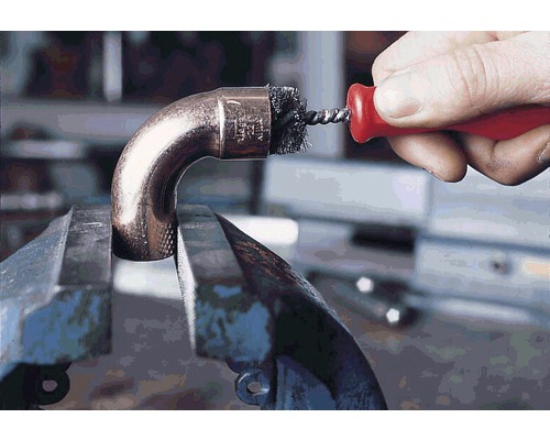 Ein Kupferrohrbogen ist in einem Schraubstock eingespannt und wird mit einer Rohrbürste gereinigt.