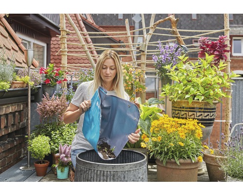 Frau leert Pflanzsack in einen Metalleimer auf einem Balkon mit vielen Pflanzen.