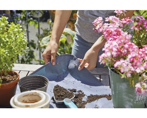 Person verwendet eine Pflanzmatte zum Umtopfen von Pflanzen im Garten.