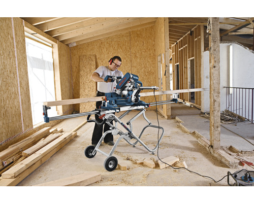 Eine Person benutzt eine Kappsäge von Bosch auf einem Montageständer in einem unfertigen Raum.