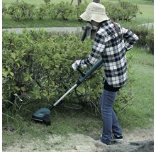 Eine Frau schneidet mit einem Akku-Rasentrimmer Gras im Garten.