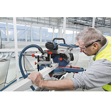 Ein Mann benutzt eine Kappsäge, um ein Werkstück zu schneiden. Er trägt eine Schutzbrille und Gehörschutz.