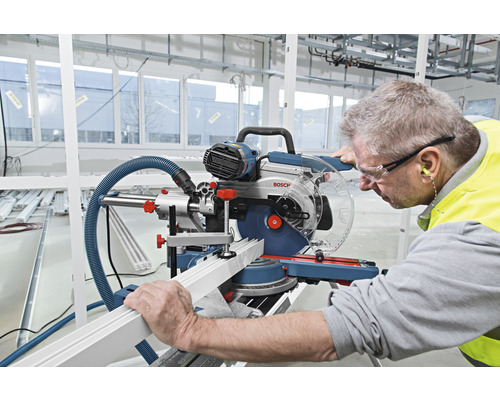 Ein Mann benutzt eine Kappsäge, um ein Werkstück zu schneiden. Er trägt eine Schutzbrille und Gehörschutz.