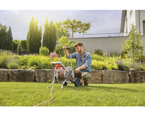 Mann benutzt einen Gartenschlauchwagen im Garten.
