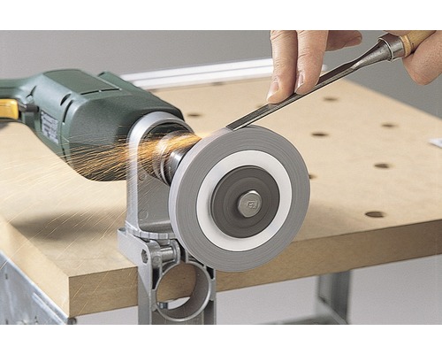 Eine Schleifscheibe ist an einer Bohrmaschine befestigt, während eine Person ein Stecheisen darauf schärft und Funken entstehen.