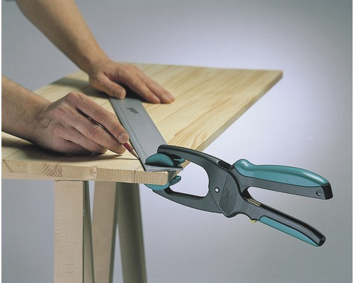 Mann markiert Holzbrett mit Bleistift und Anschlagwinkel, fixiert mit Einhandzwinge auf Tisch