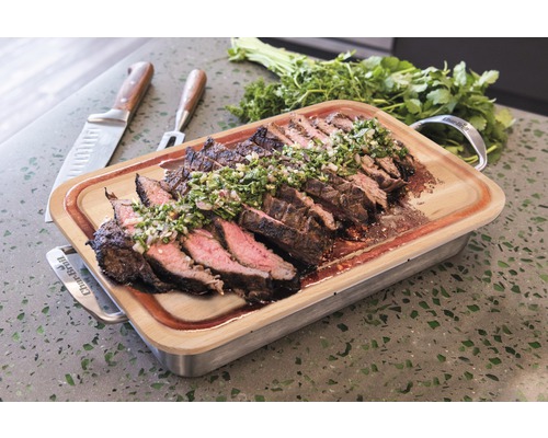 Geschnittenes Steak mit Kräutern auf einem Schneidebrett mit Griffen.
