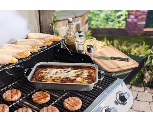Grillszene mit Maiskolben, Auflaufform, Burgerbratlingen, Schneidebrett, Messer, Gewürzen und Saucen auf einem Grill
