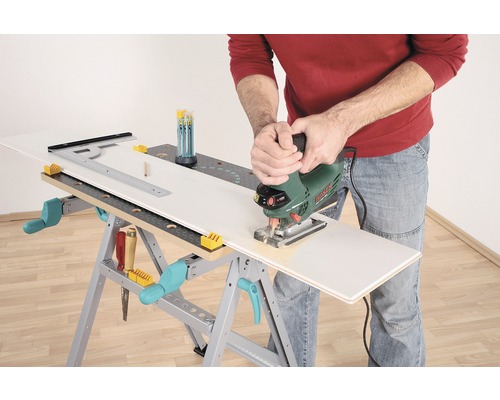 Eine Person schneidet mit einer Stichsäge ein Werkstück auf einer Werkbank.