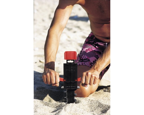 Mann befestigt Sonnenschirm mit einer Eindreh-Bodenhülse im Sand