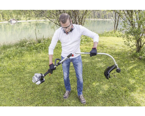 Mann montiert einen Rasentrimmer im Garten in der Nähe eines Sees