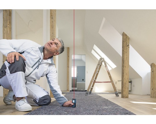 Handwerker benutzt einen Laser-Entfernungsmesser in einem Dachgeschoss, um präzise Messungen durchzuführen.