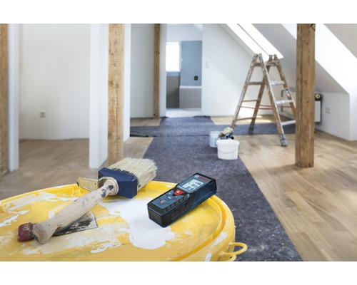 Raumrenovierung mit Laser-Entfernungsmesser, Farbe und Pinsel auf einem Eimer