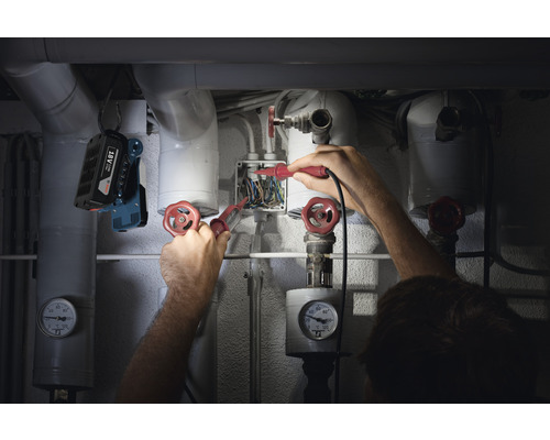 Ein Installateur arbeitet mit Spannungsprüfern an einem Verteilerkasten, beleuchtet von einer Arbeitsleuchte.