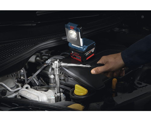 Akku-Arbeitsleuchte im Einsatz am Automotor mit Handwerker, der einen Schraubenschlüssel benutzt