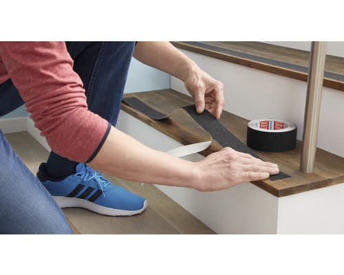 Eine Person befestigt Antirutschband auf einer Treppenstufe zur Erhöhung der Sicherheit.