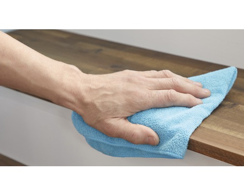 Eine Hand wischt mit einem Reinigungstuch über eine Holzoberfläche.