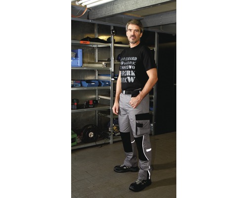 Mann trägt Arbeitshose vor einem Regal