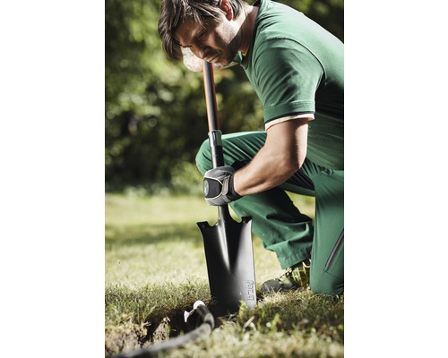 Ein Mann kniet im Garten und gräbt mit einem Spaten ein Loch.