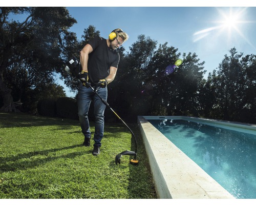 Mann trimmt Rasen mit einem Rasentrimmer in der Nähe eines Pools.