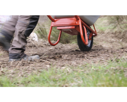 Eine Person schiebt eine Schubkarre auf unebenem Gelände.