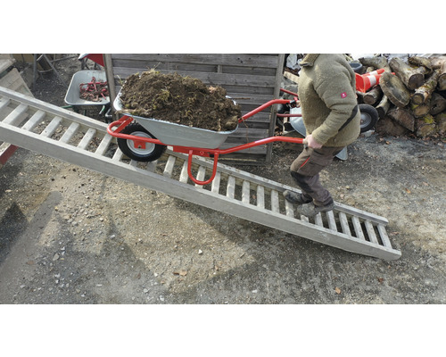 Mann schiebt Schubkarre mit Erde über eine Rampe.