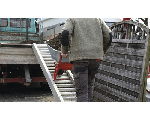 Eine Person schiebt eine Schubkarre voller Erde über eine Rampe auf einen Lastwagen.